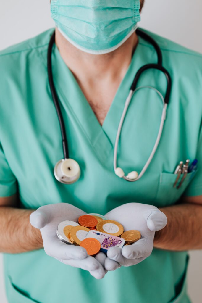 Arzt im Kittel mit Stethoskop und Schokogeldmünzen in der Hand